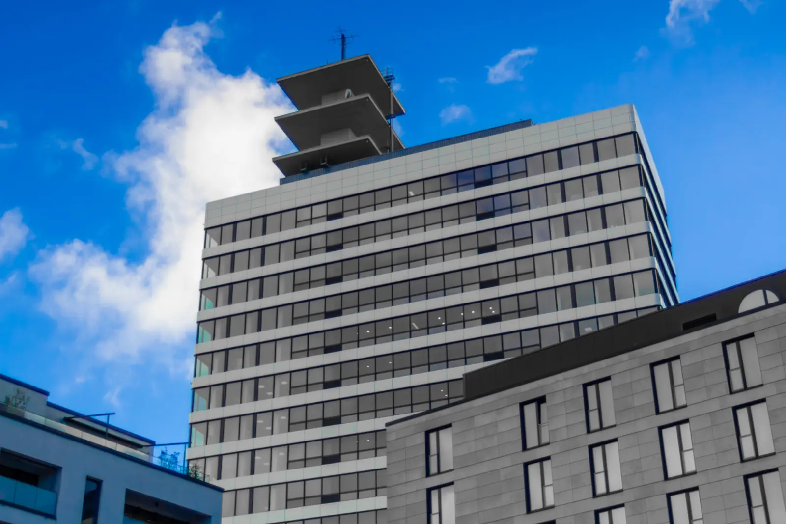 Ein modernes Bürohochhaus mit einer abgestuften Dachkonstruktion und Glasfenstern, das sich vor einem blauen Himmel mit einigen Wolken abhebt, ragt in Bielefeld markant empor.
