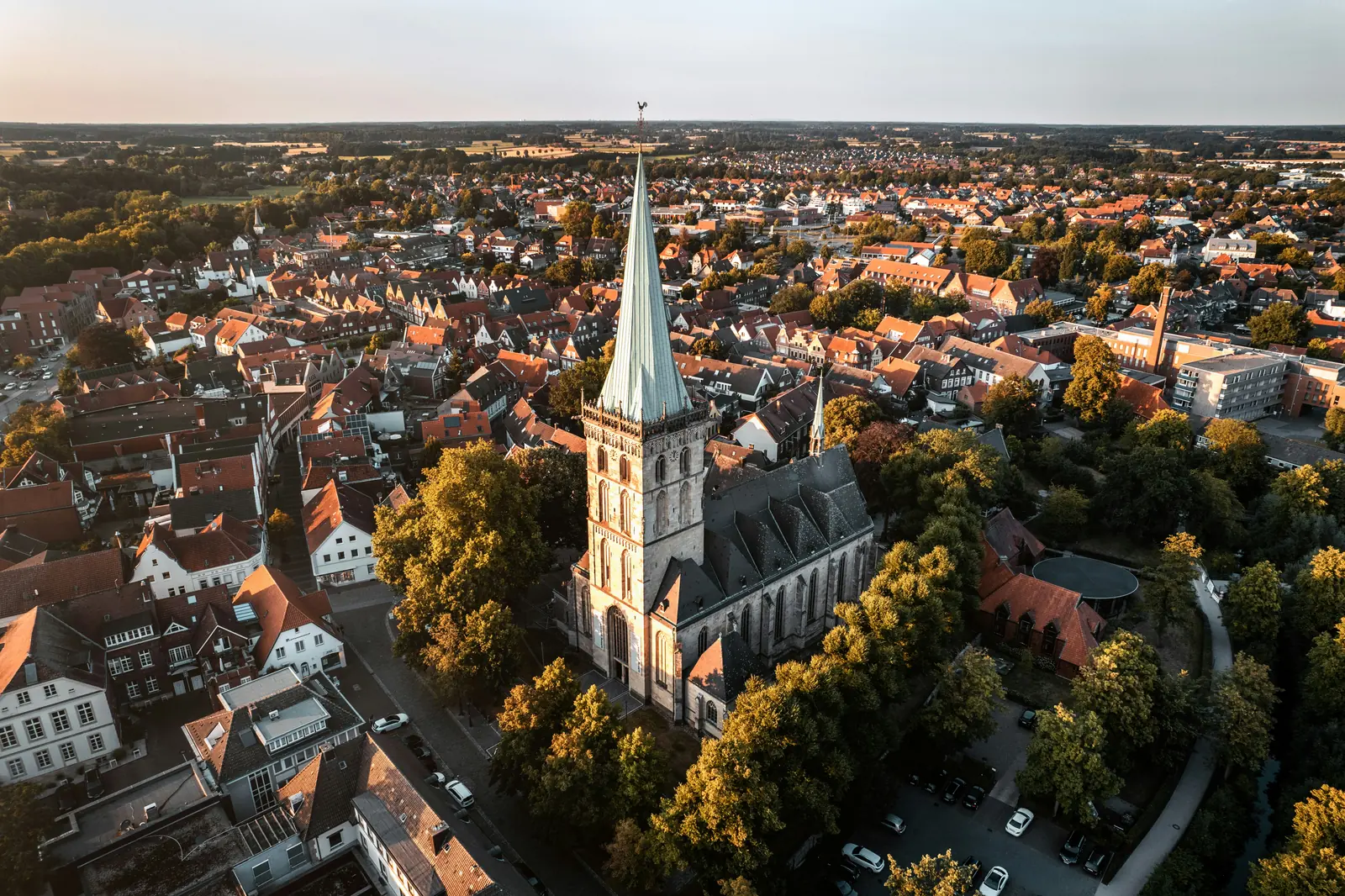 Luftaufnahme einer Kirche mit hohem Turm, der an die Kirchen in Münster erinnert, umgeben von Bäumen und Wohnhäusern in einer Kleinstadt bei Tageslicht; das Bild fängt sowohl den architektonischen Charme als auch die geordnete Umgebung ein, die typisch für Gebiete sind, in denen die Standards der Betriebsmittelprüfung eingehalten werden.