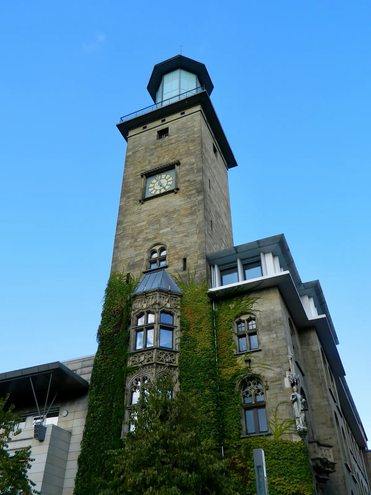 Turm des Alten Rathauses in Hagen mit Uhr, verglastem Aufsatz und efeubewachsener Fassade.