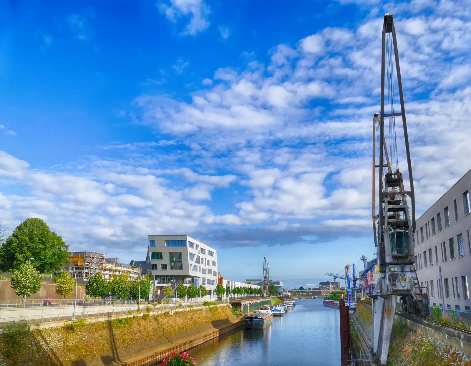 Hafenbecken in Neuss mit altem Kran, Binnenschiffen und modernen Gebäuden.