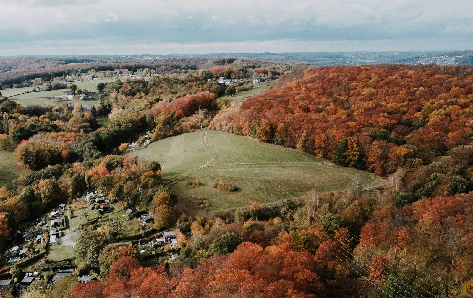 Luftaufnahme einer herbstlichen Hügellandschaft mit Wiesen, Wäldern und Gärten am Stadtrand von Hagen.