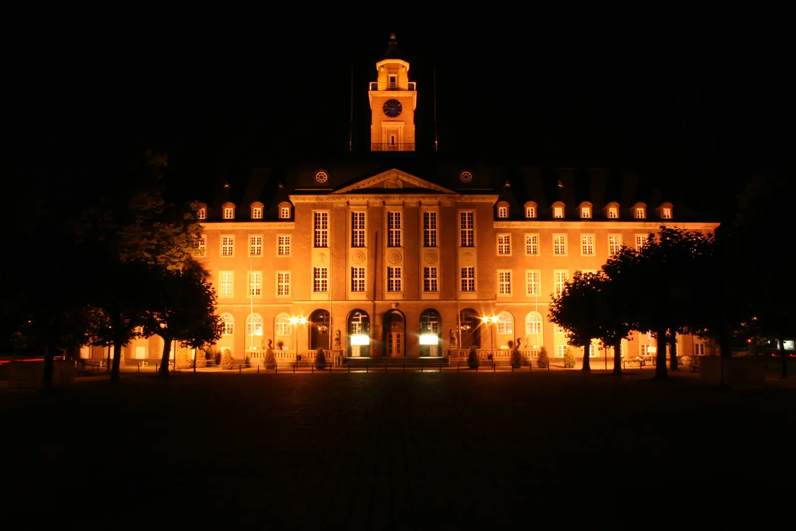 Nachts beleuchtetes Rathaus Herne mit Uhrturm und Vorplatz.