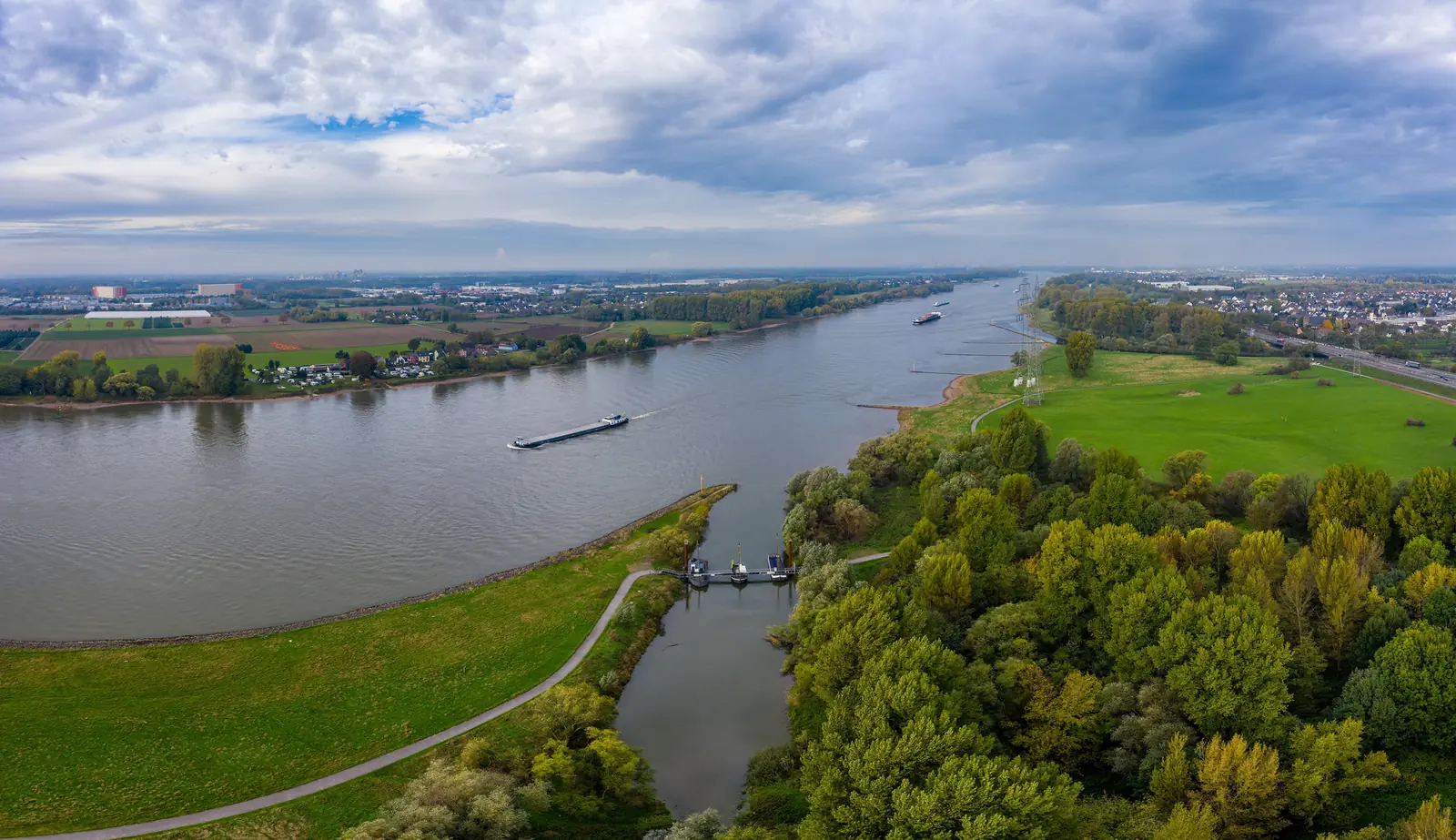Luftaufnahme des Rheins bei Leverkusen mit Frachtschiff und grünen Uferwiesen.