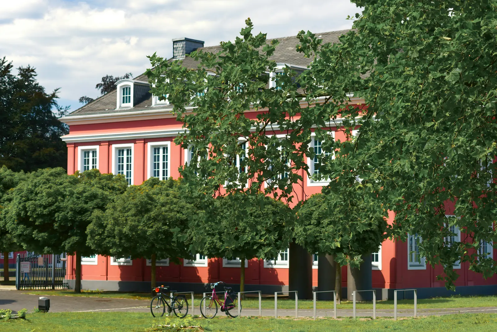 Schloss Oberhausen, klassizistisches Gebäude mit rosa Fassade hinter grünen Bäumen.