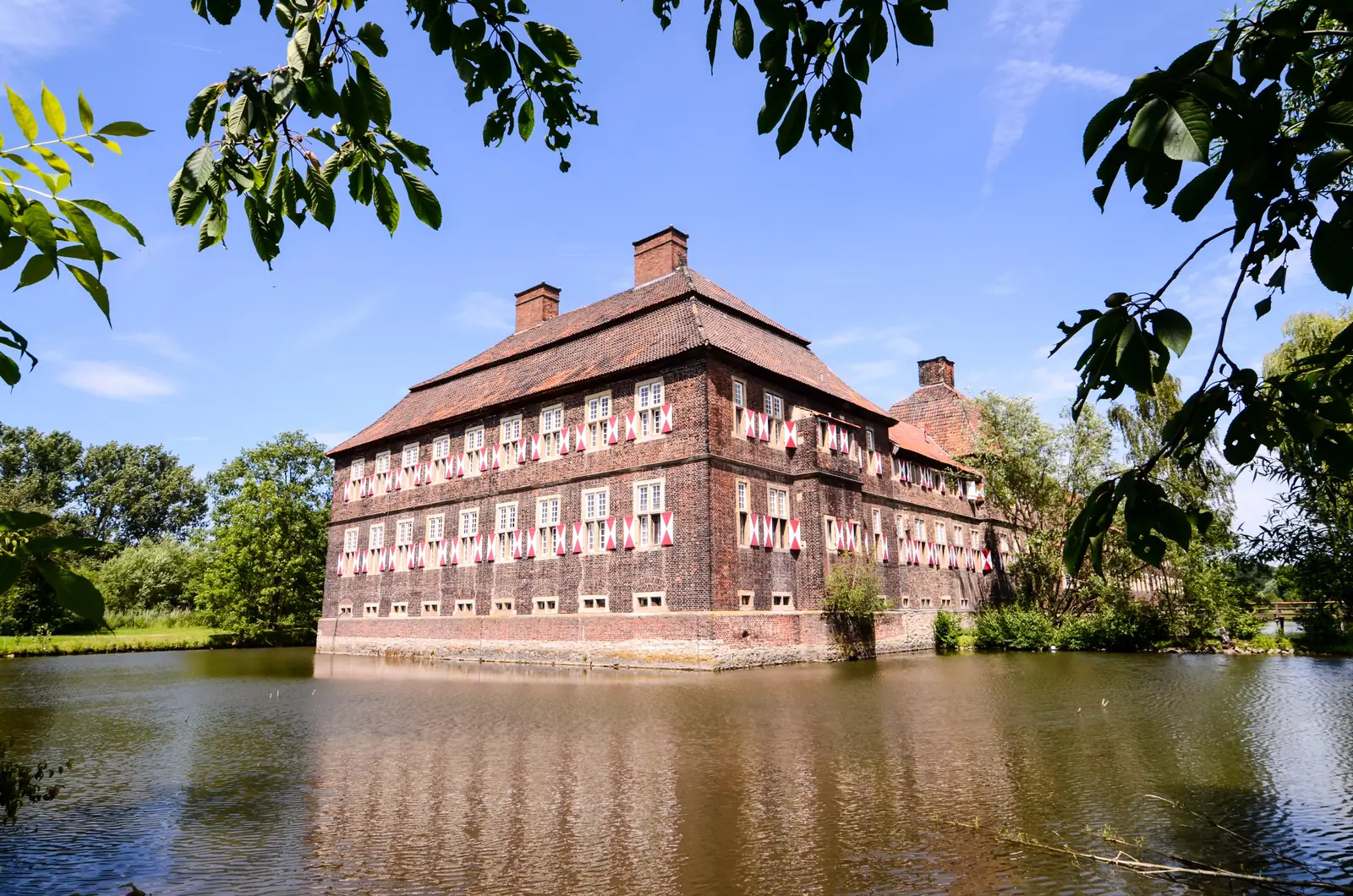 Herrenhaus von Schloss Oberwerries mit rot-weißen Fensterläden hinter dem Wassergraben.