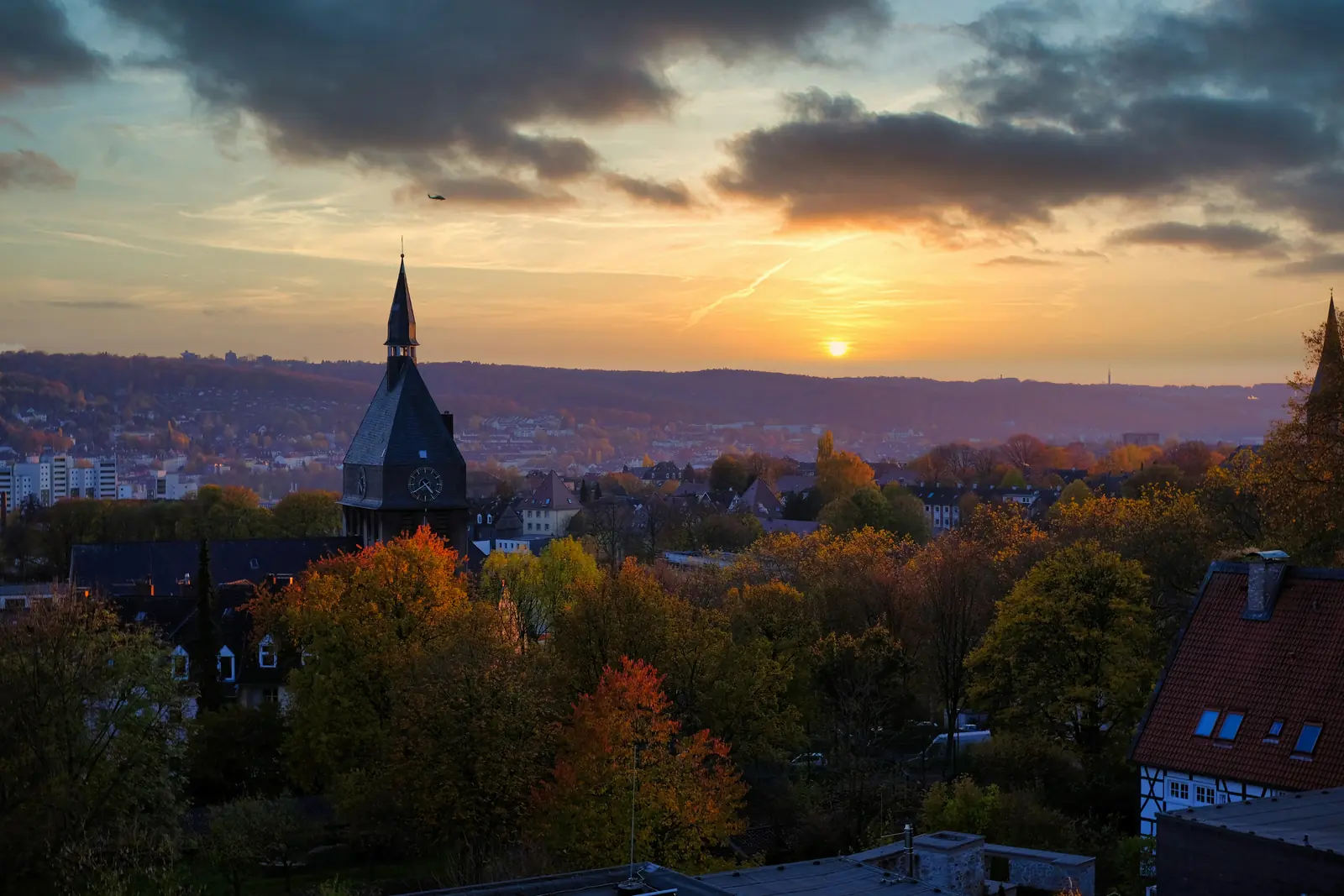 Sonnenuntergang über Wuppertal mit Kirchturm und herbstlich gefärbten Bäumen.