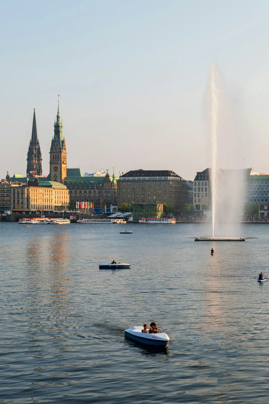 Alsterfontäne auf der Binnenalster in Hamburg mit Tretbooten und Rathausturm.