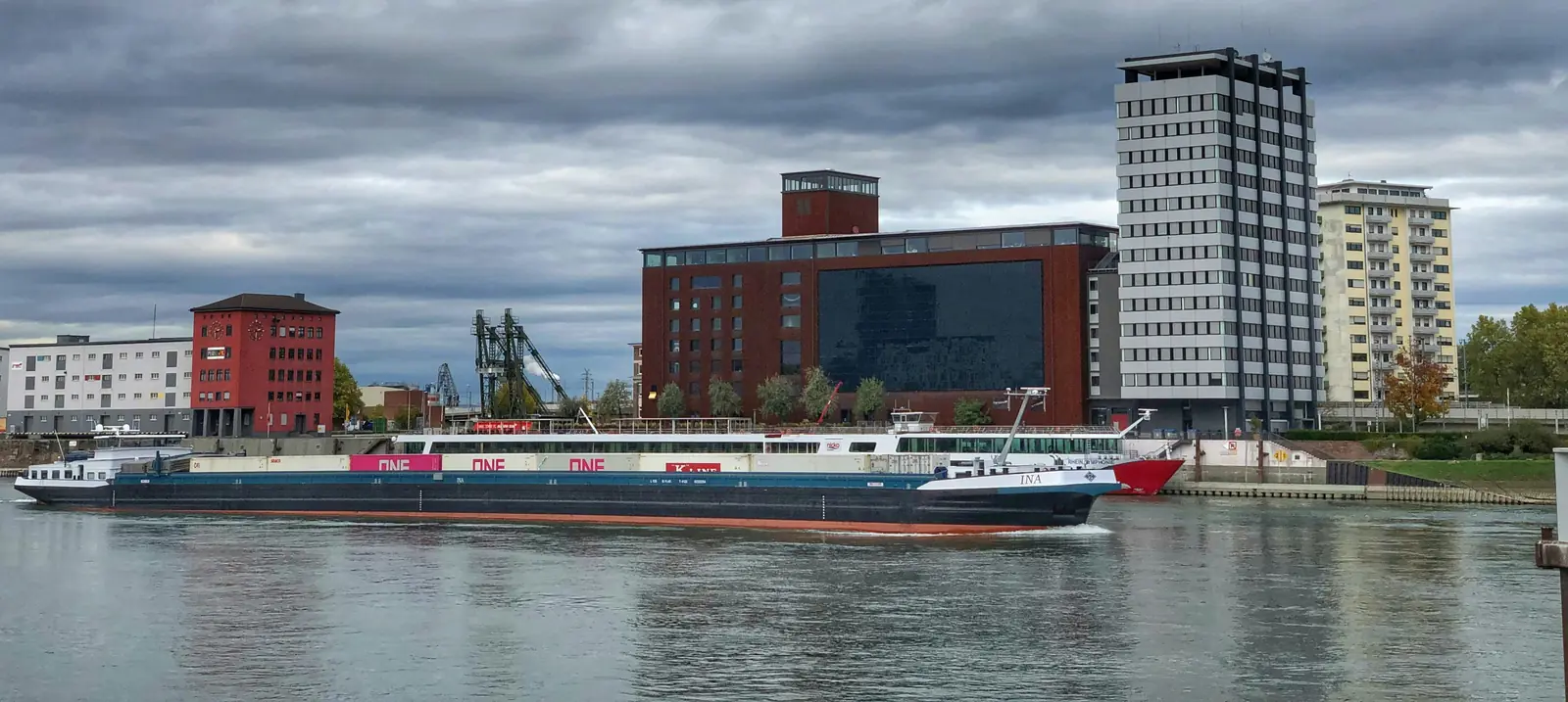 Frachtschiff am Rheinufer in Ludwigshafen vor Bürogebäuden und einem Hochhaus.