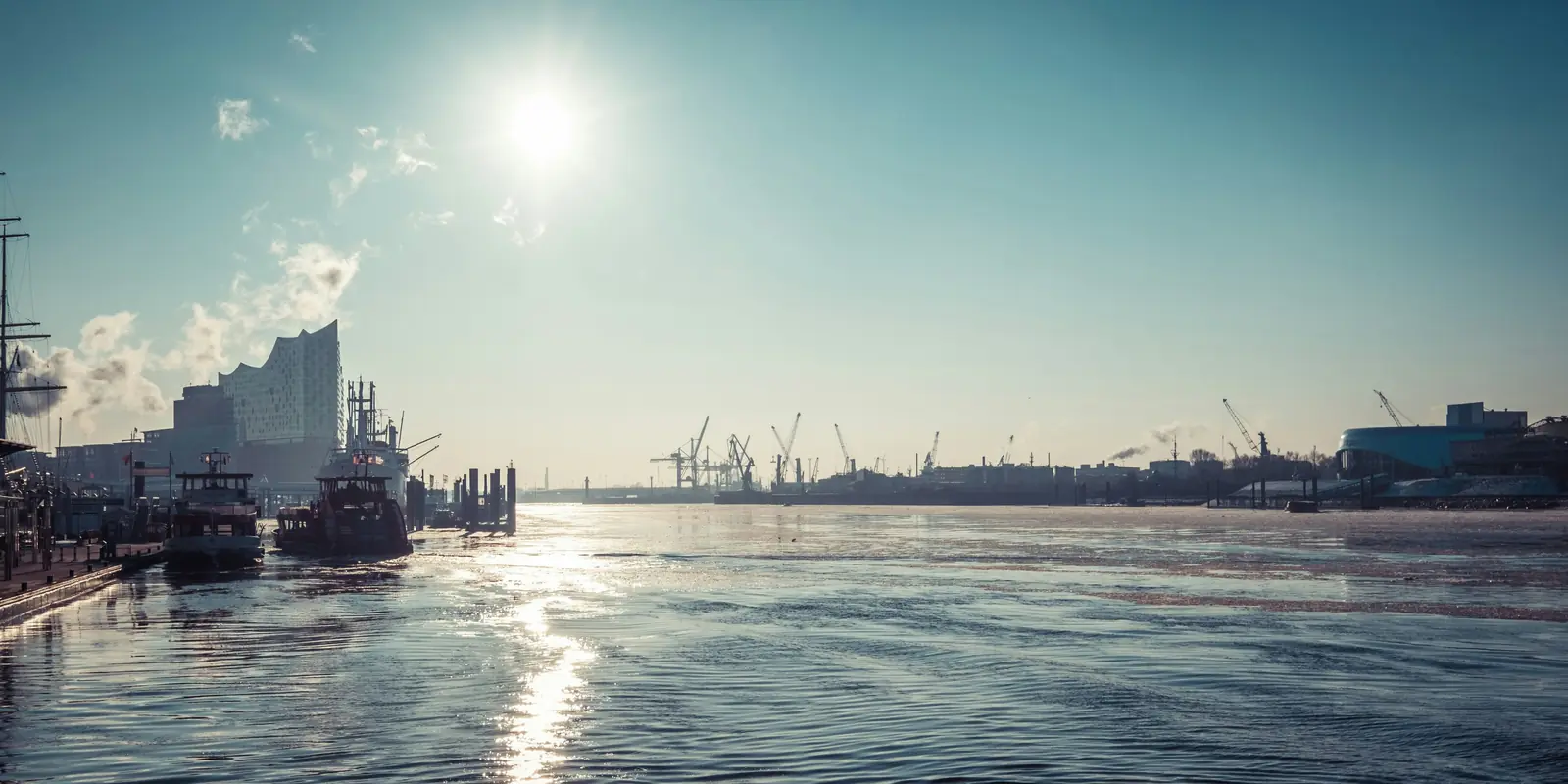 Gegenlicht über dem Hamburger Hafen mit Hafenkränen und der Elbphilharmonie.