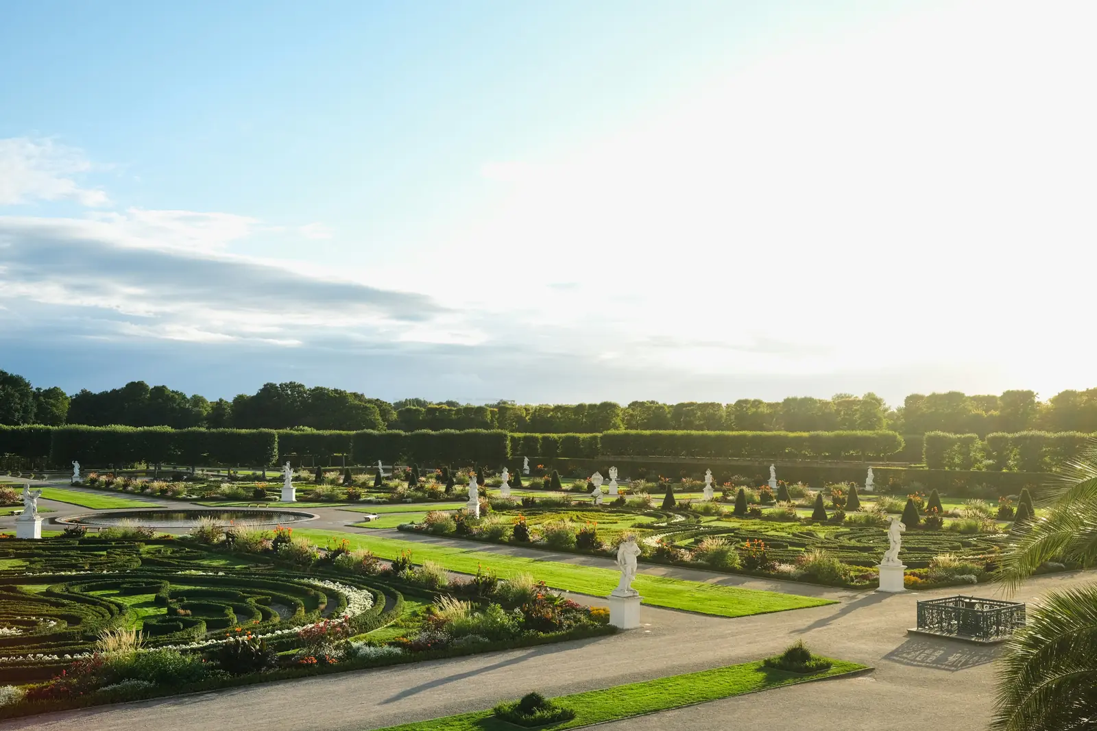 Großer Garten in Herrenhausen in Hannover mit Barockornamenten und Skulpturen im Abendlicht.