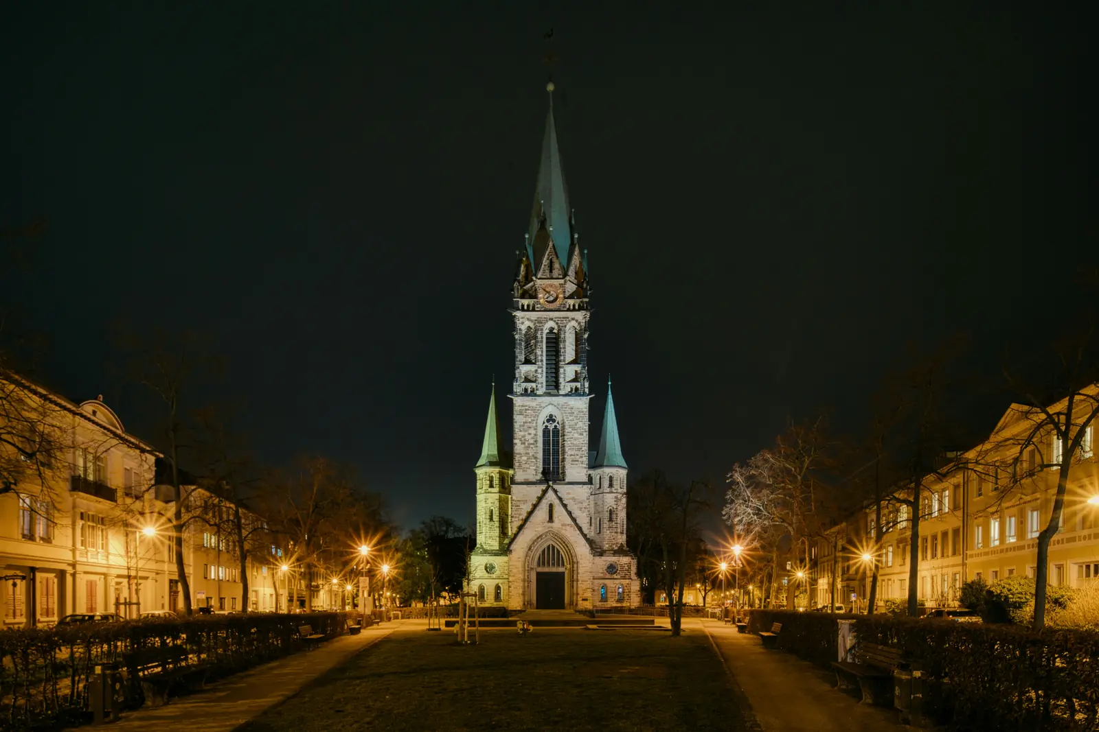 Nachts beleuchtete Johanneskirche in Darmstadt am Ende einer Allee.