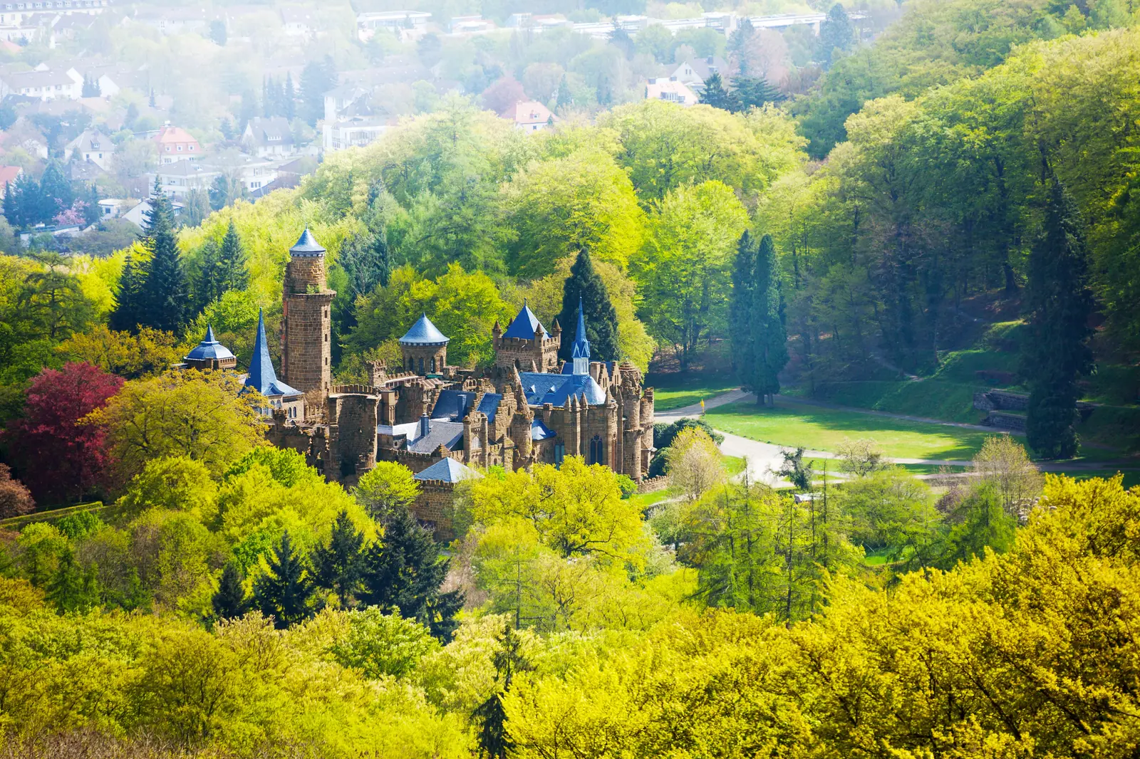 Löwenburg mit blauen Turmdächern zwischen den Frühlingswäldern des Bergparks Wilhelmshöhe.