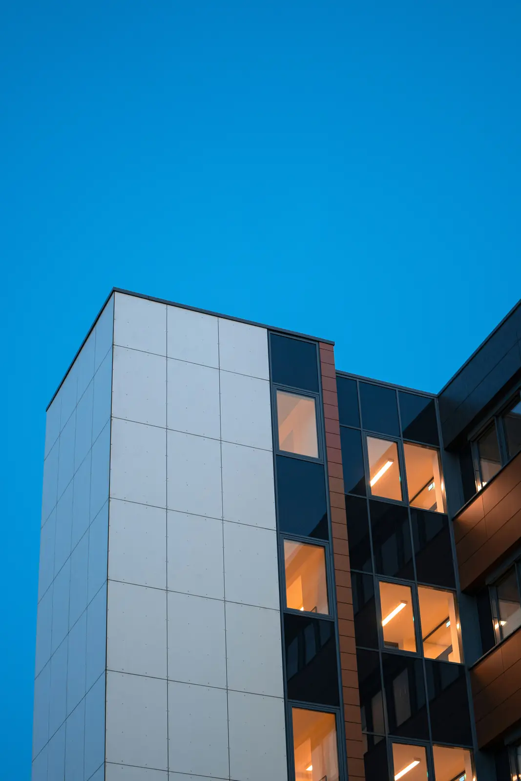 Moderne Gebäudeecke in Oldenburg mit beleuchteten Fenstern in der blauen Stunde.