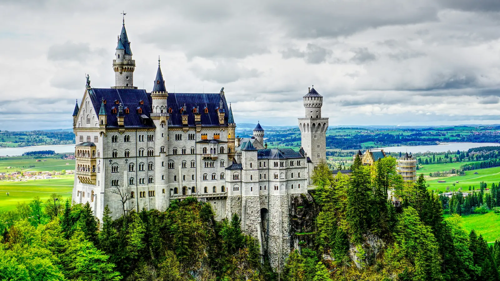 Schloss Neuschwanstein im Allgäu auf einem Felsen über bewaldeten Hügeln.