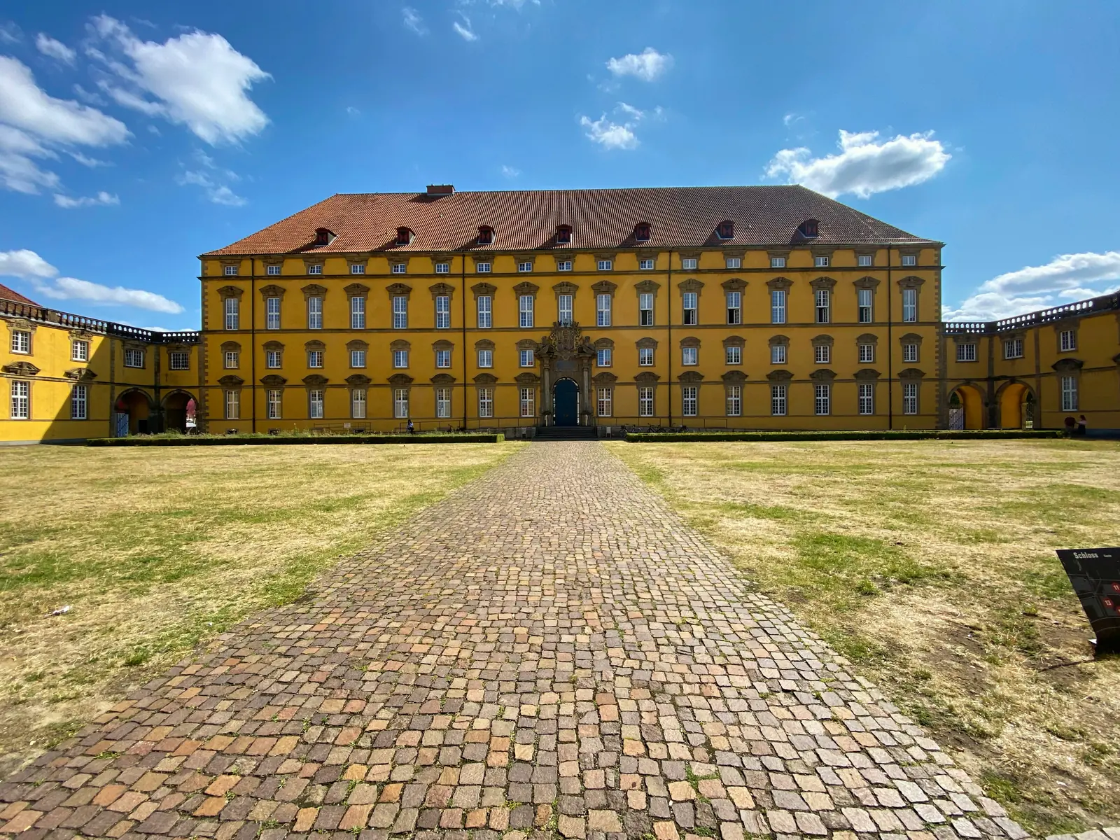 Schloss Osnabrück, gelber Barockbau mit Kopfsteinpflasterweg im Innenhof.