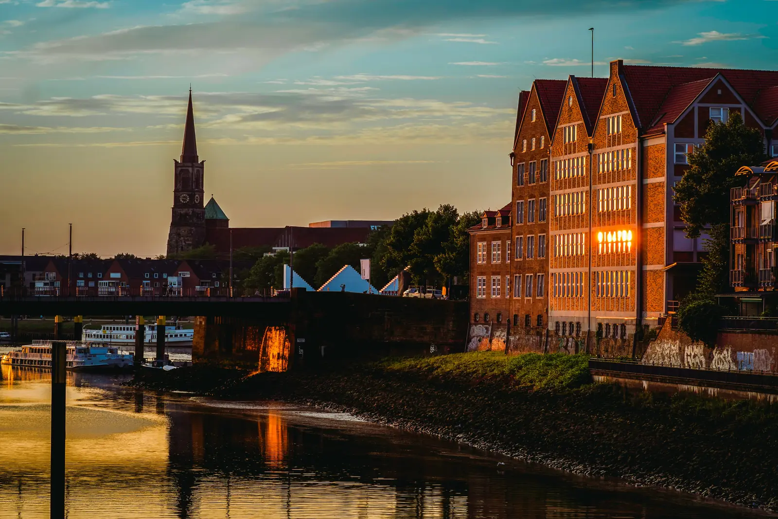 Sonnenuntergang an der Weser in Bremen mit Backsteinspeichern und einem Kirchturm.