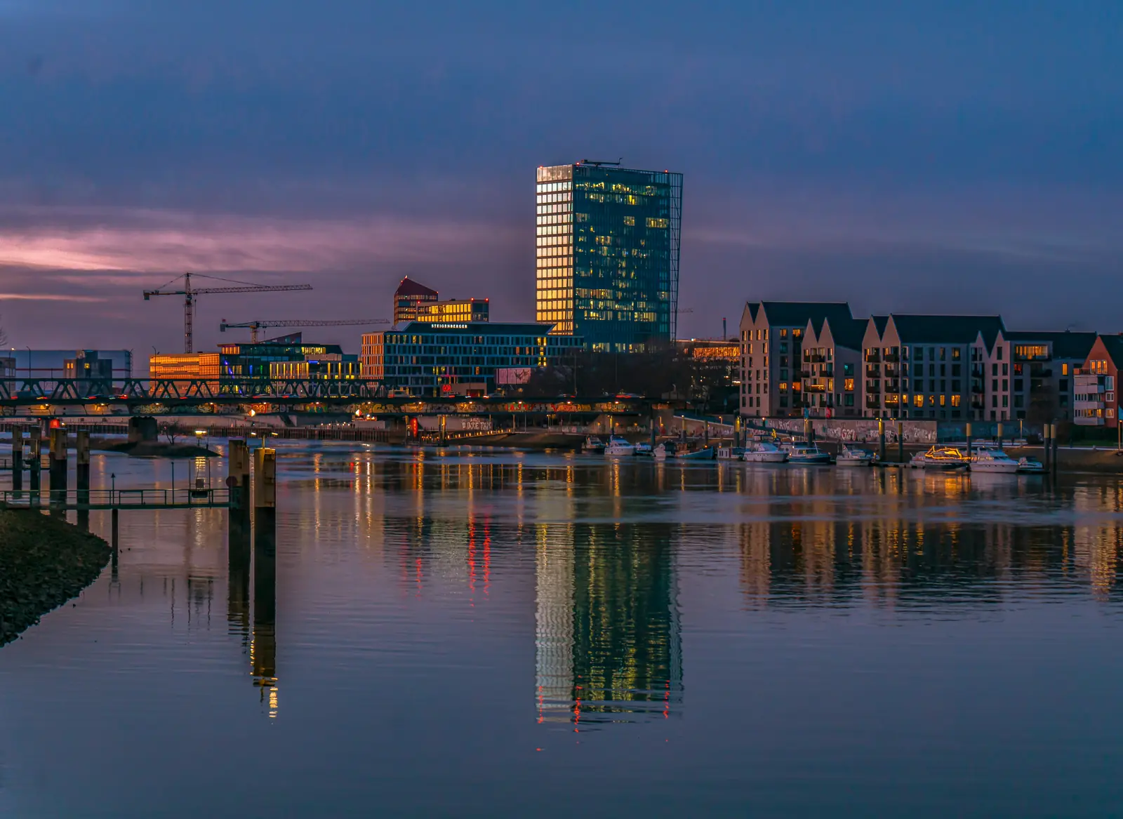 Weser Tower in der Bremer Überseestadt spiegelt sich abends in der Weser.