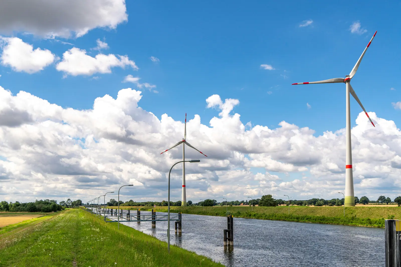 Windräder an einem Kanal in der flachen Landschaft Niedersachsens.