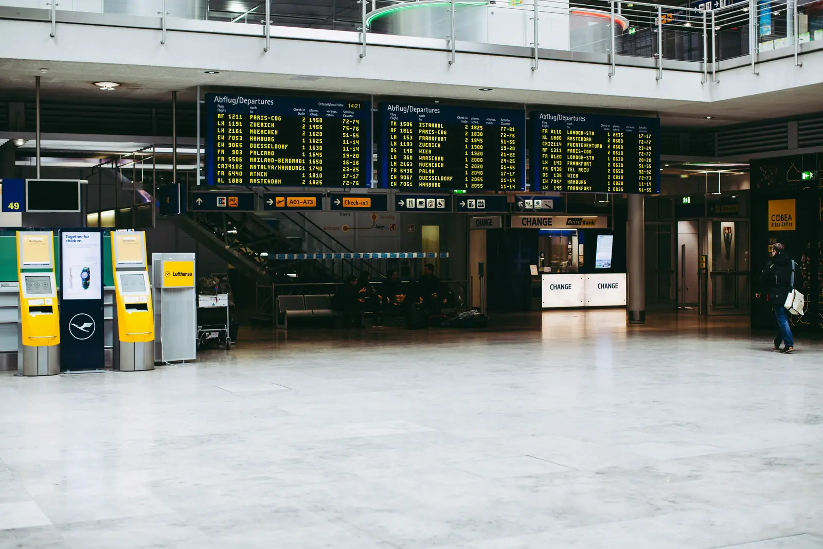 Betriebsmittelprüfung am Flughafen: Abflugtafeln und Check-in-Automaten in der Halle.