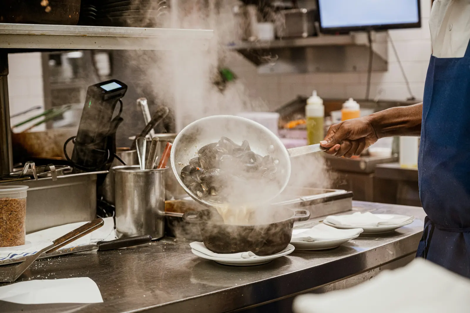 Betriebsmittelprüfung und Leiter- und Trittprüfung im Catering: Koch schüttet dampfende Muscheln um.