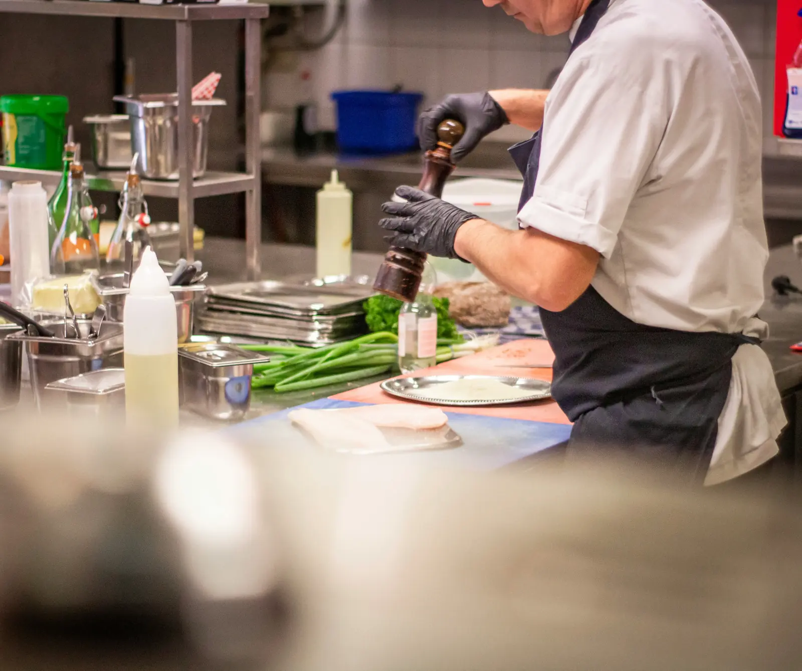 Betriebsmittelprüfung und Leiter- und Trittprüfung im Catering: Koch würzt am Vorbereitungstisch.