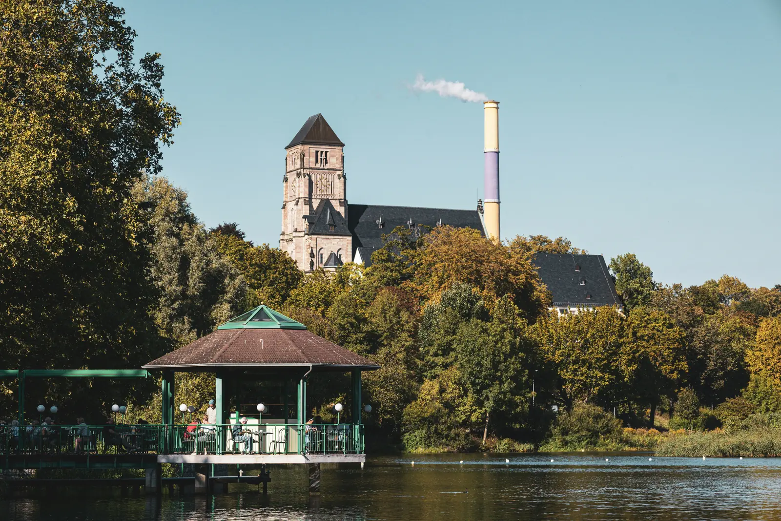 Betriebsmittelprüfung und Leiter- und Trittprüfung in Chemnitz: Pavillon am Wasser vor Kirche und Schornstein.