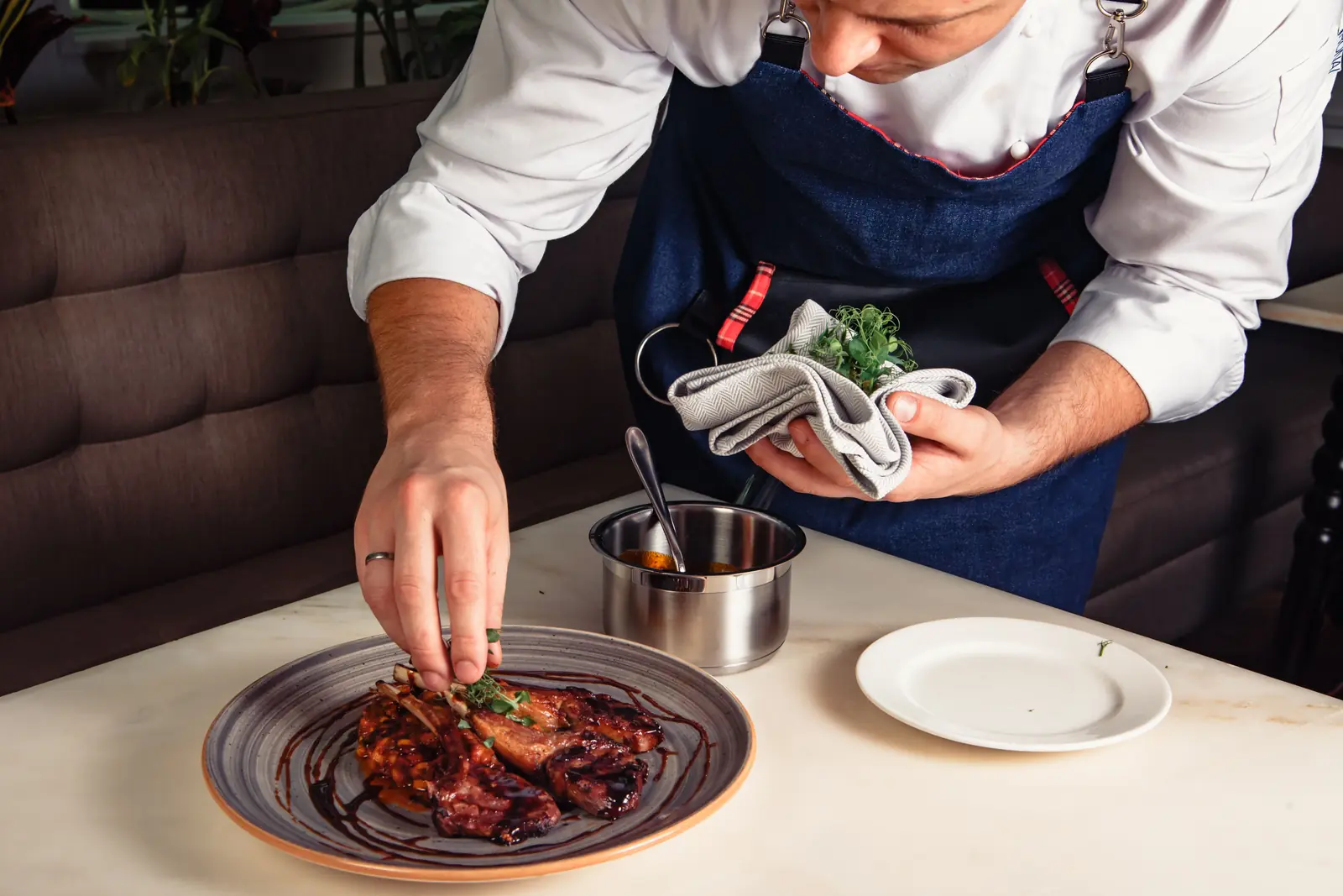 Betriebsmittelprüfung und Leiter- und Trittprüfung in der Gastronomie: Koch richtet einen Teller am Tisch an.