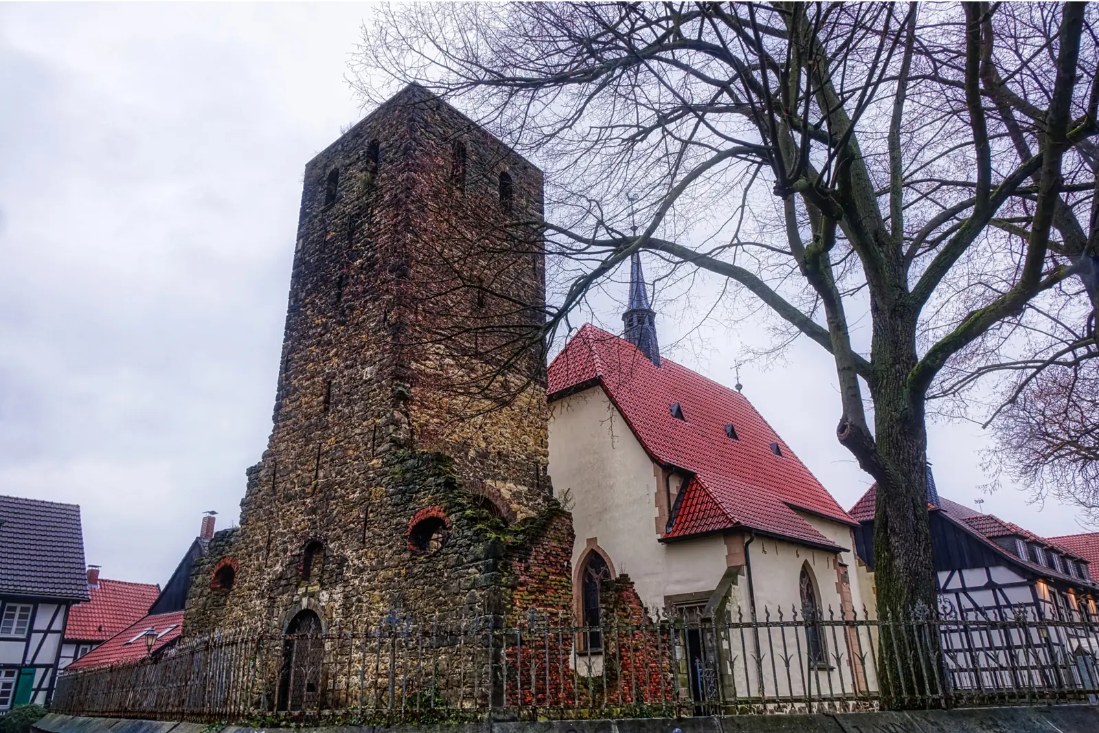 Betriebsmittelprüfung und Leiter- und Trittprüfung in Herten: Efeubewachsener Kirchturm neben rotem Ziegeldach.
