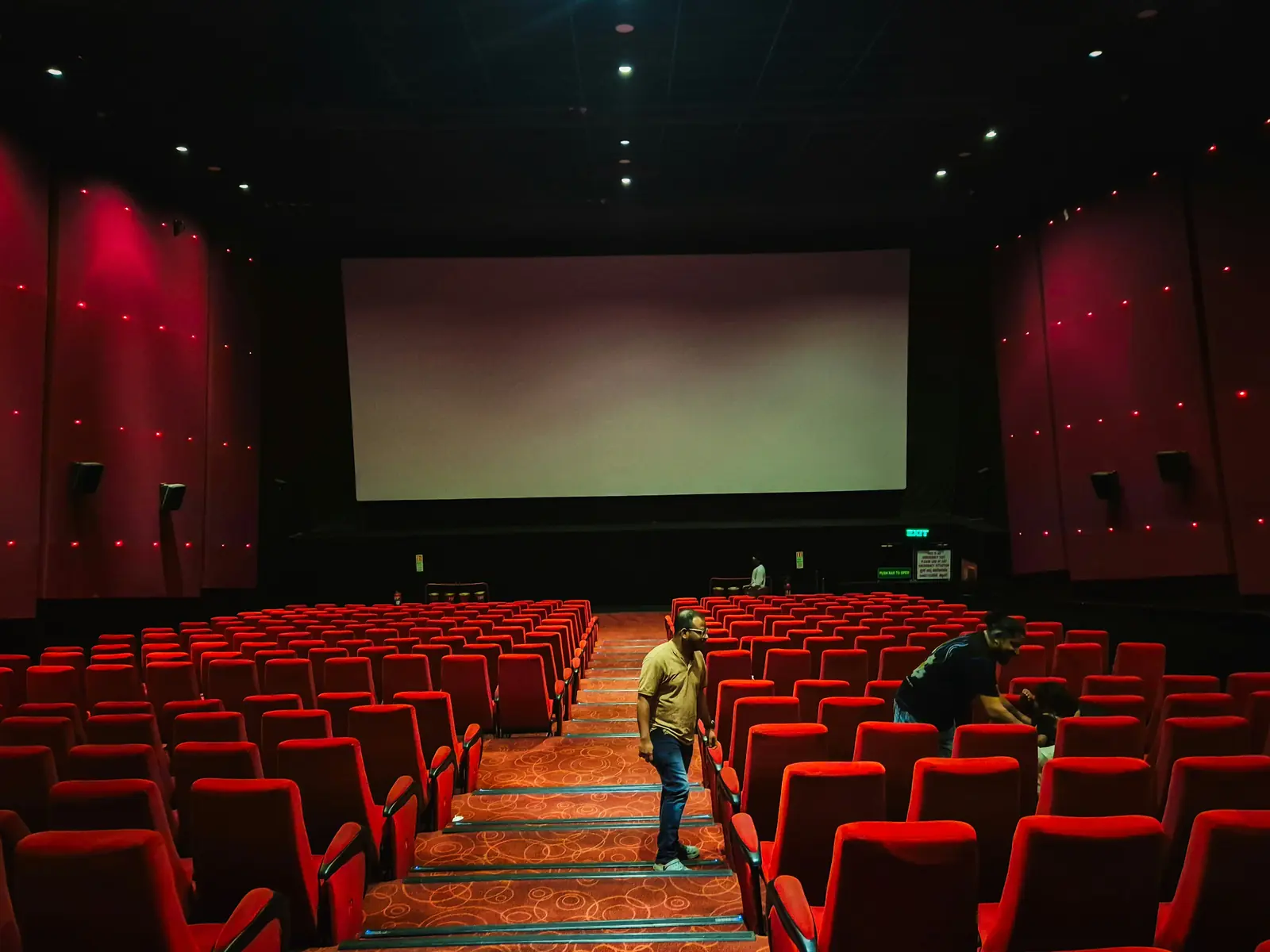 Betriebsmittelprüfung und Leiter- und Trittprüfung im Kino: Personal reinigt die Sitzreihen vor der Leinwand.