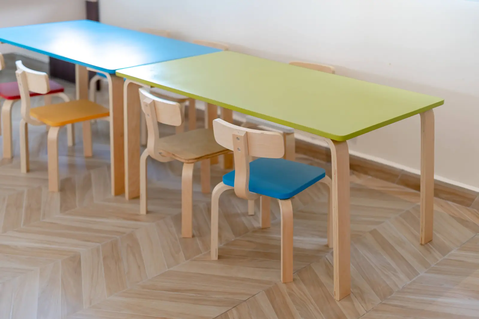 Betriebsmittelprüfung und Leiter- und Trittprüfung in der Kita: Bunte Kindertische mit Holzstühlen.