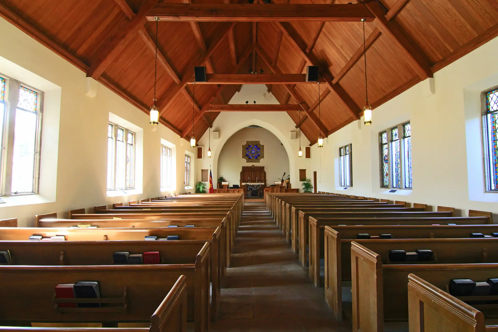 Leiter- und Trittprüfung in der Kirche: Holzdachstuhl mit Hängeleuchten über den Bänken.