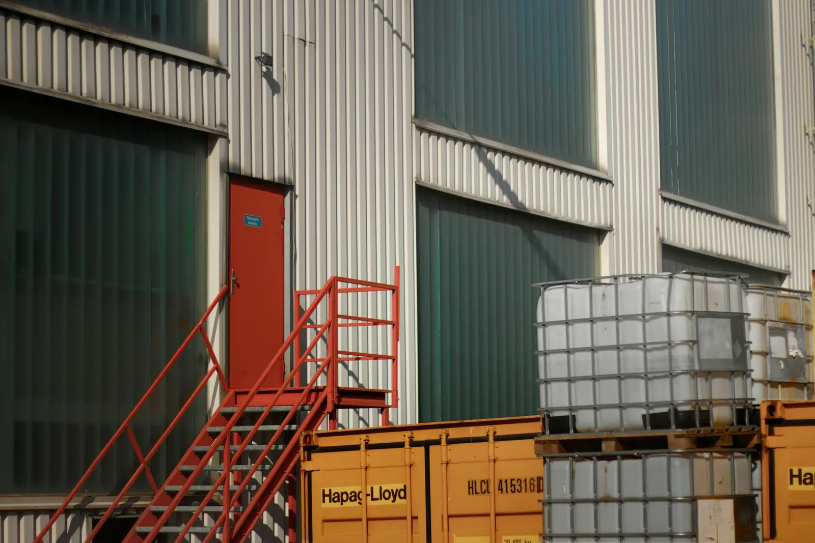 Leiter- und Trittprüfung im Lager: Rote Außentreppe an der Halle über Containern.