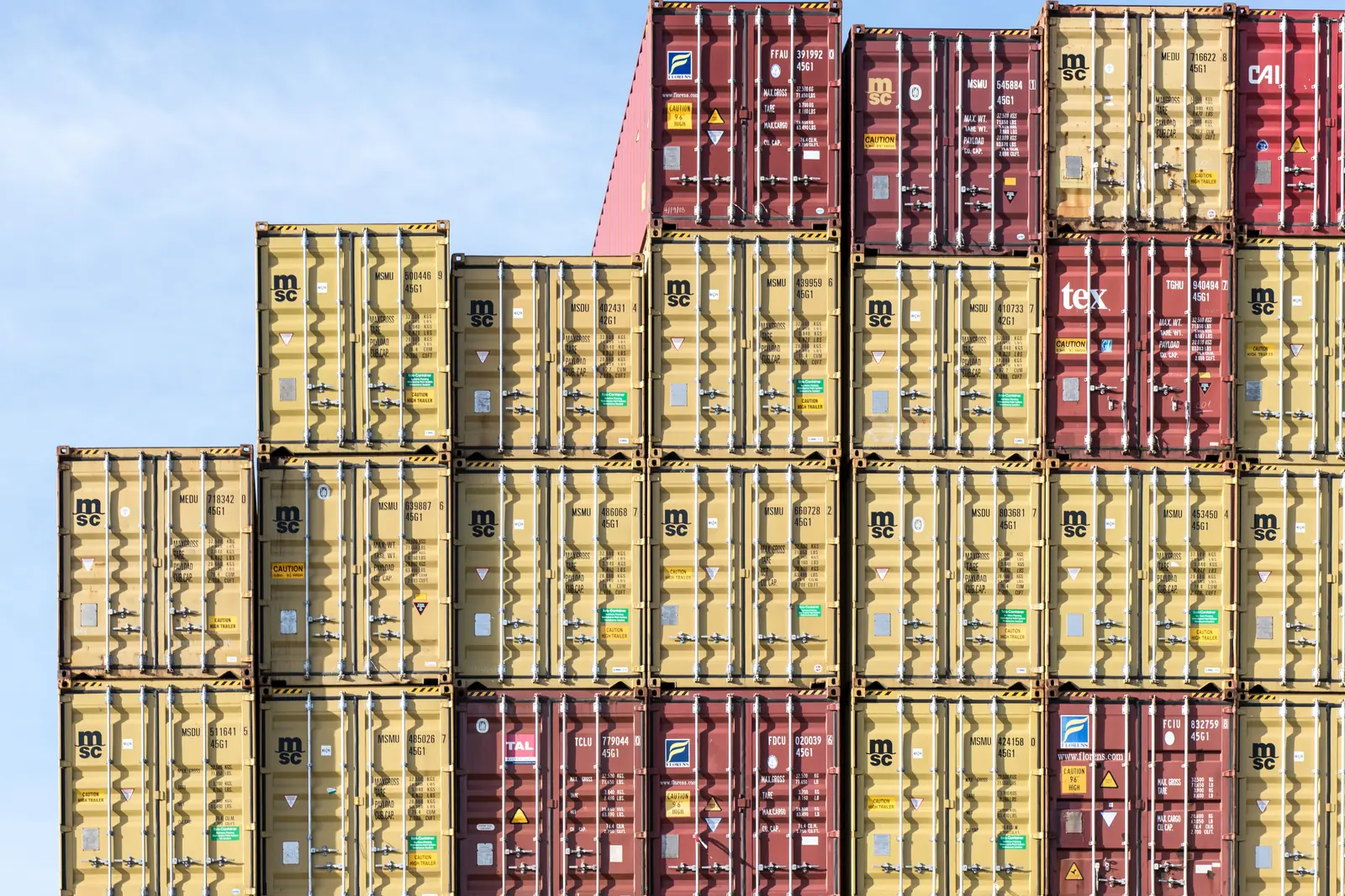 Leiter- und Trittprüfung in der Spedition: Hoch gestapelte Container vor blauem Himmel.