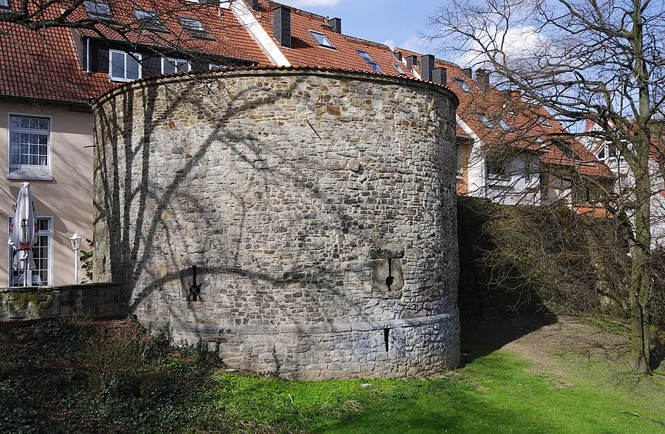 Leiter- und Trittprüfung in Unna: Runder Wehrturm aus Bruchstein hinter Wohnhäusern.