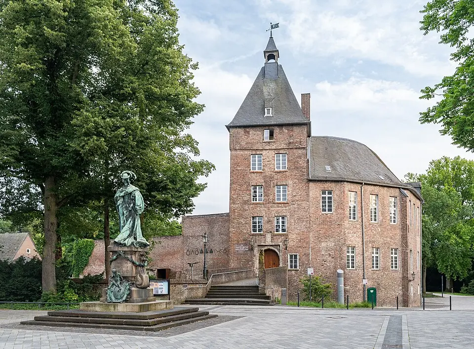 Betriebsmittelprüfung und Leiter- und Trittprüfung in Moers: Backsteinschloss mit Denkmal davor.
