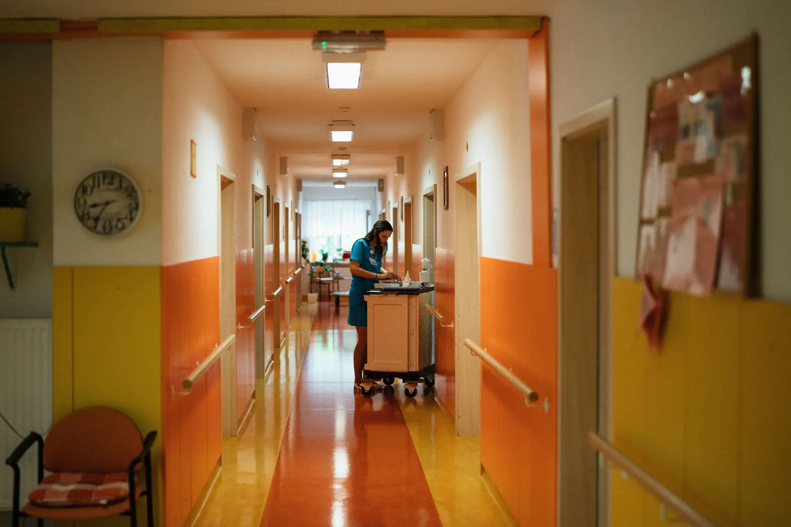 Betriebsmittelprüfung und Leiter- und Trittprüfung im Pflegeheim: Pflegekraft mit Wagen im beleuchteten Flur.
