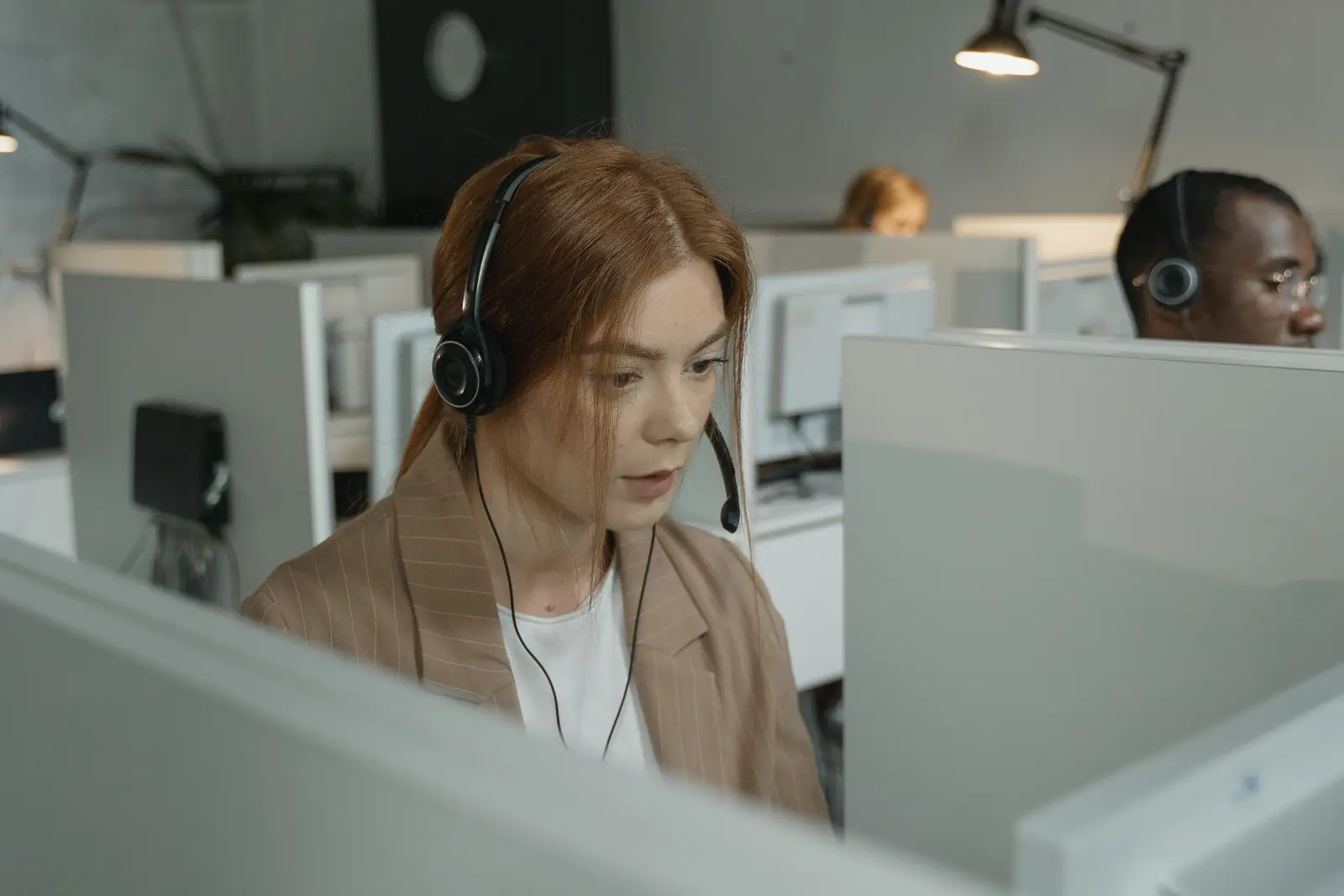 Betriebsmittelprüfung und Leiter- und Trittprüfung im Callcenter: Mitarbeiterin mit Headset in einer Arbeitsplatzkabine.