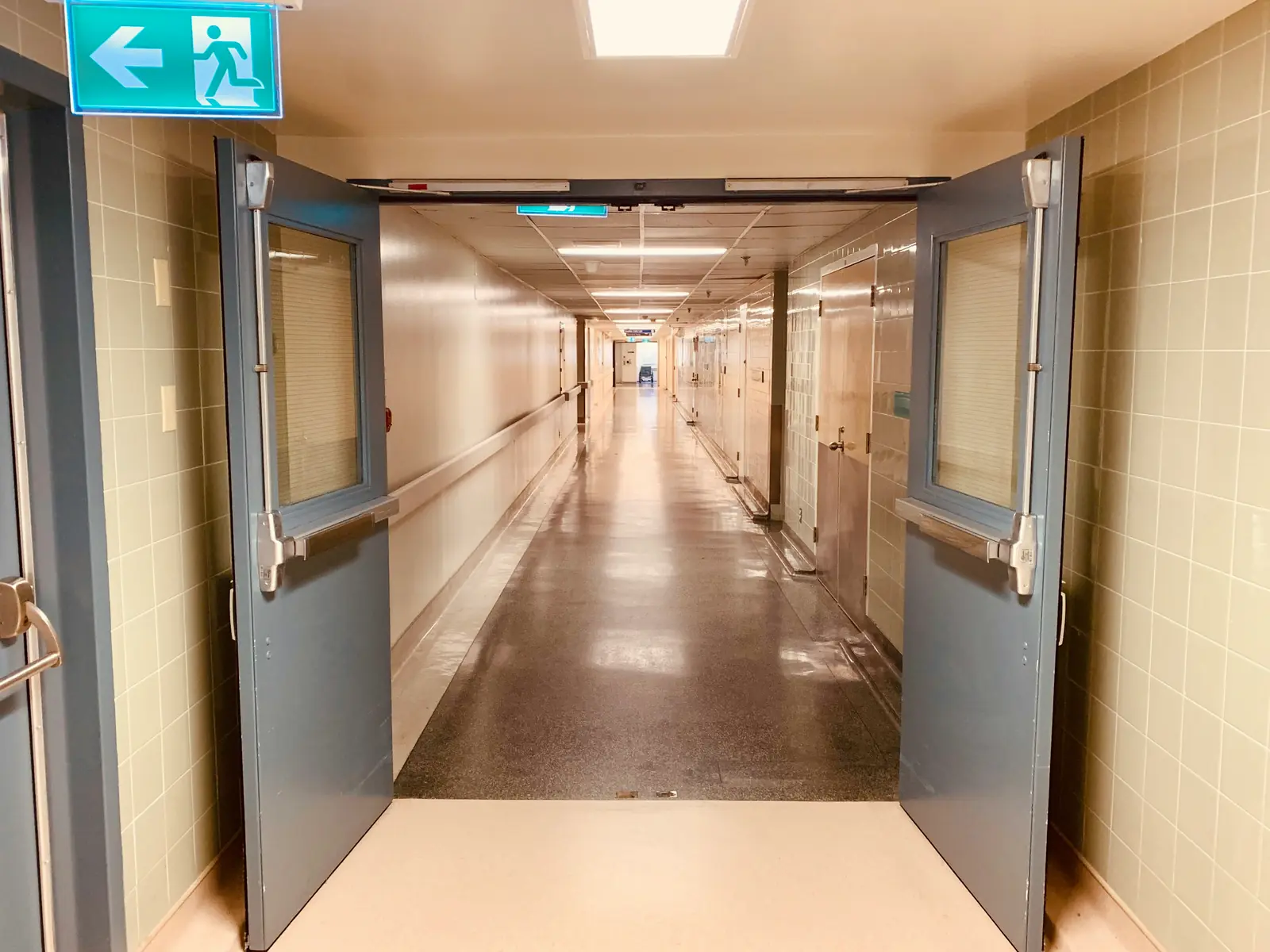 Betriebsmittelprüfung und Leiter- und Trittprüfung im Krankenhaus: Stationsflur mit Brandschutztüren und Notausgangsschild.