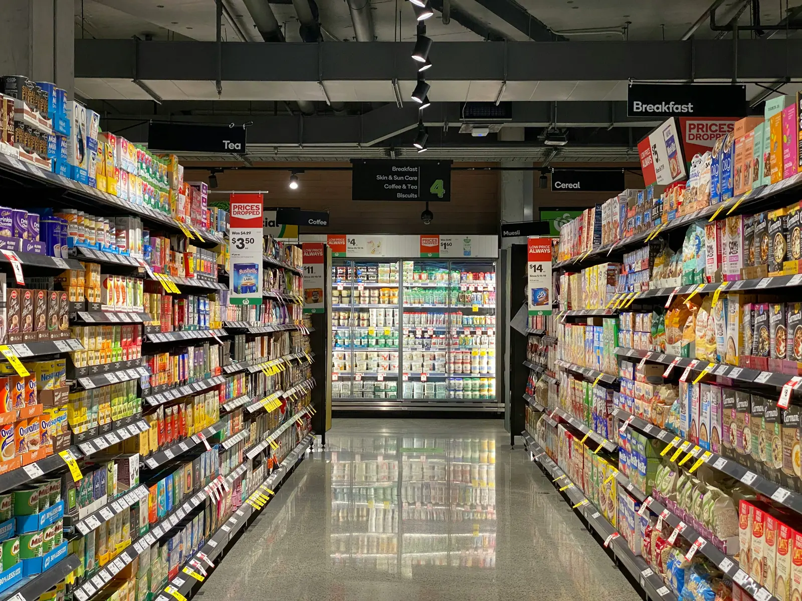 Betriebsmittelprüfung und Leiter- und Trittprüfung im Supermarkt: Gang zwischen hohen Regalen bis zur Kühltheke.