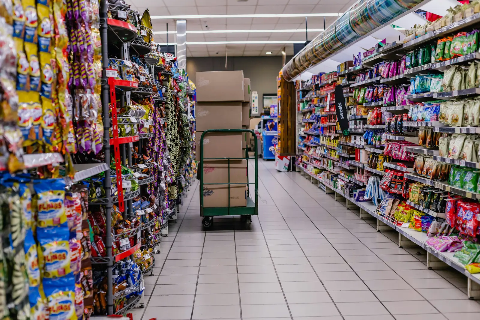 Betriebsmittelprüfung und Leiter- und Trittprüfung im Supermarkt: Verkaufsgang mit Rollwagen und Nachschubkartons.