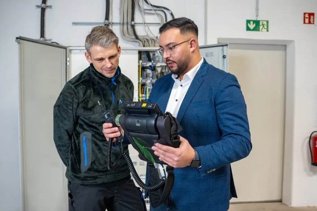 Zwei Männer schauen in einer Garage in eine Kamera.